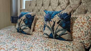 A bed with floral bedding and two decorative pillows, a tufted headboard, and a window with a view of the outside.