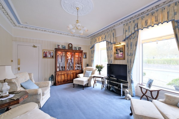 A spacious living room with a large television, comfortable seating, a wooden cabinet, and a view of the outdoors. - The Jays Guest House (Aberdeen)