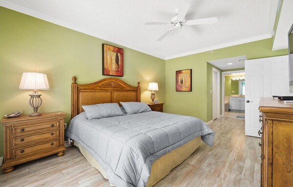 A bedroom with a bed, wooden nightstands, a ceiling fan, and artwork on the walls.