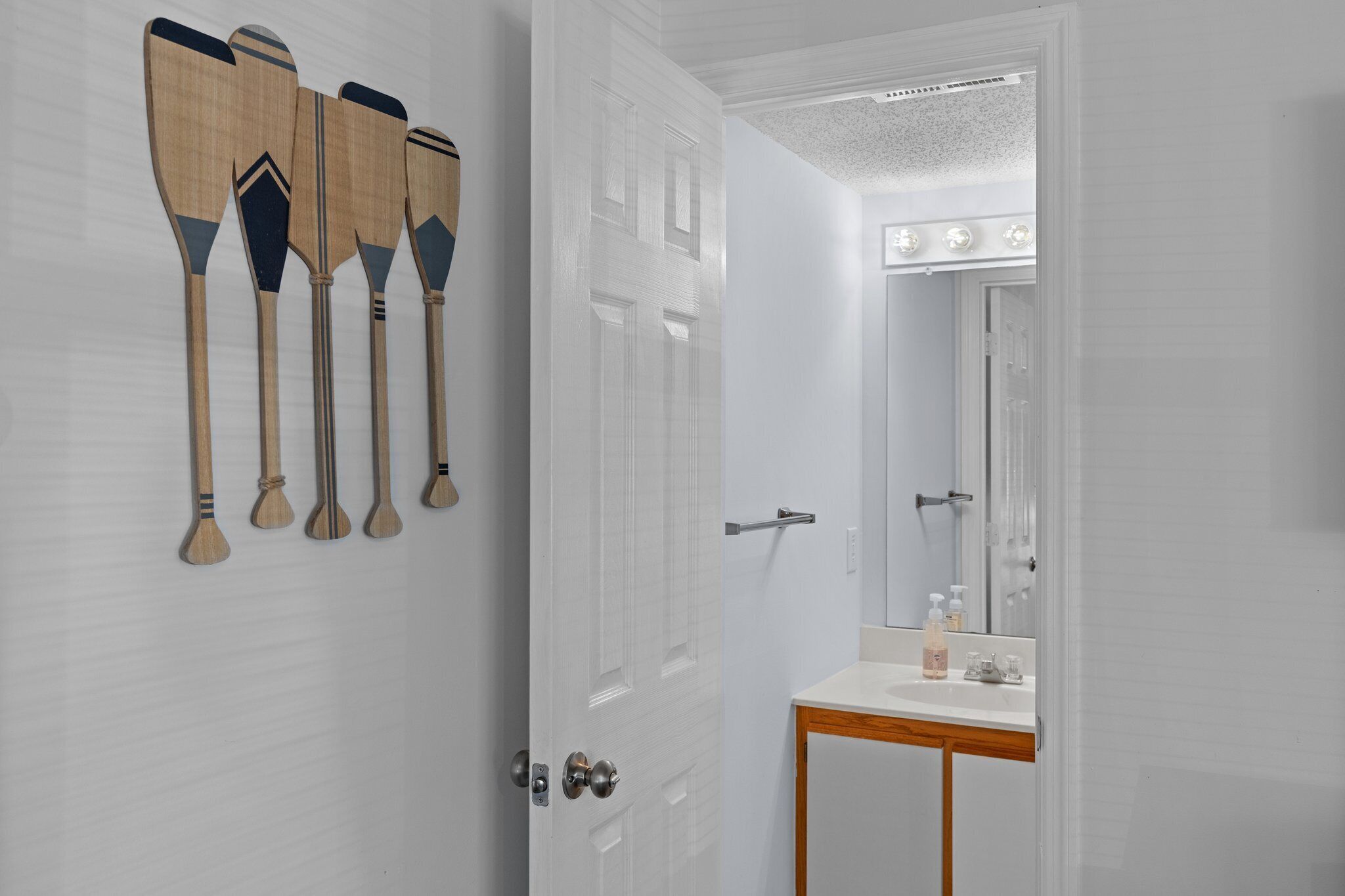 A bathroom with a white door, a mirror, a sink, and wooden paddles on the wall.