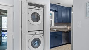A laundry room with two white front-loading washers and a blue kitchen with a dishwasher. - Sleeps 5! 2 BR, 2.5BA Townhome-Walk to Beach & Dining – Your Escape Awaits! (Emerald Isle)