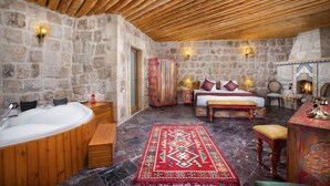 Ein Zimmer mit Steinwänden und Holzbalkendecke, einer großen Badewanne, einem Bett mit Kissen, einer Bank und einem Tisch mit Dekoration.