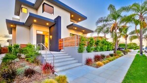 A modern two-story house with a staircase leading to the entrance, surrounded by landscaped gardens and palm trees. - Rooftop Deck/Ocean Views/A/C/Close To All (La Jolla)