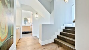 A modern interior with a staircase, wooden flooring, and a hallway leading to a kitchen area. - Rooftop Deck/Ocean Views/A/C/Close To All (La Jolla)