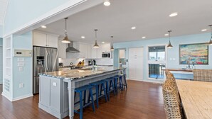 Una cocina amplia con una isla central, taburetes de bar e iluminación colgante.