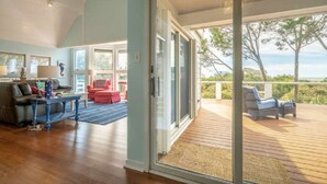 Amplia sala de estar con un gran ventanal corredizo que da a una terraza de madera con mobiliario exterior.