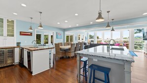 Cocina amplia con una isla central, muebles blancos y un comedor con sillas de mimbre.