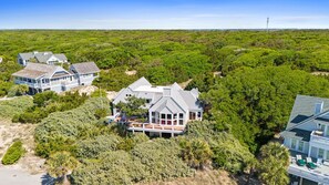 Een groot, tweelaags huis met een veranda die eromheen loopt, omringd door weelderige begroeiing en een strand op de achtergrond.