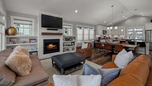 A modern living room with a fireplace, a television, and a dining area with a kitchen in the background. - Seabrook Play Among Stars | Hot Tub, Ocean View | Pet Friendly, 4BR, Sleeps 8 (Pacific Beach)