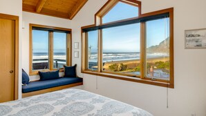 A bedroom with a large bed, a built-in bench with cushions, and a view of the ocean through large windows.