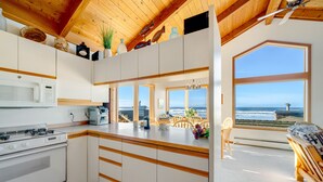 A modern kitchen with white cabinets, a stove, and a view of the ocean through large windows.