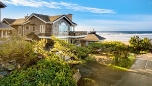 A coastal house with a balcony overlooking the beach, surrounded by lush greenery.