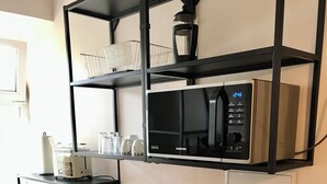 Una cocina compacta con encimera negra, microondas, hervidor y fregadero.
