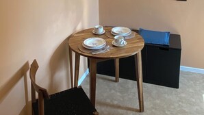 Un pequeño comedor con una mesa redonda para cuatro personas, una lámpara colgante de mimbre, un banco con cojín negro y una silla con asiento negro.