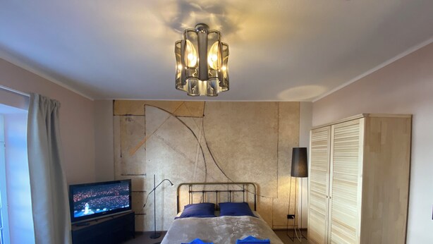 Un dormitorio con cama, televisión, candelabro, armario y una pared con diseño texturizado.