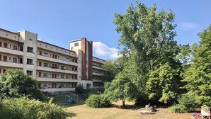 Un edificio de varios pisos con una chimenea central, rodeado de un área verde con bancos y juegos infantiles.