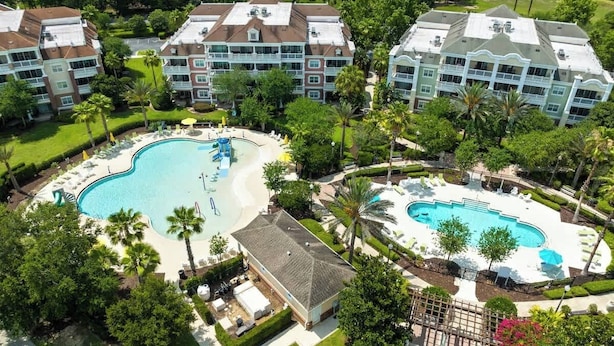 Un hotel con una amplia piscina central, varios balcones y un exuberante paisaje.