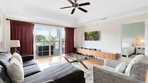 Una sala de estar moderna con sofá, sillón, mesa de centro de vidrio y ventilador de techo.