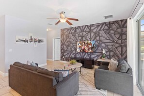 Een moderne woonkamer met een bank, fauteuils, een salontafel en een televisie die aan een gestructureerde muur is bevestigd.