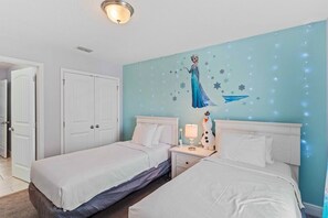 Een slaapkamer met twee bedden, witte beddengoed, een nachtkastje met een lamp en een muurschildering van een personage.