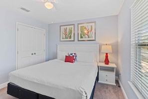 Een slaapkamer met een bed, een nachtkastje, een lamp en twee foto's die aan de muur hangen.