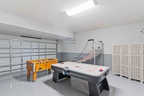 Een schone, overdekte recreatieruimte met een tafelvoetbaltafel, een biljarttafel en een kleine, gele pingpongtafel.