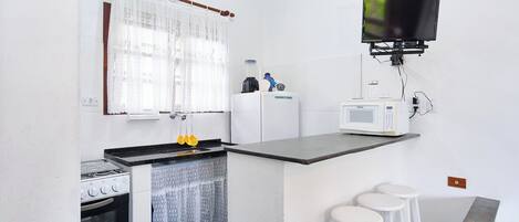 A compact kitchen with a stove, microwave, and bar stools.