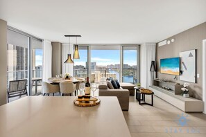 A modern hotel room with a dining area, a sofa, a TV, and a city view.