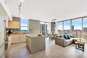 Um apartamento moderno com cozinha, sala de jantar e sala de estar. Possui janelas amplas com vista para a cidade.