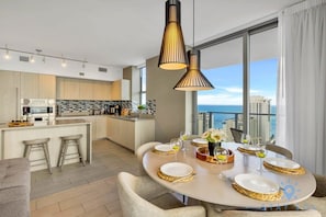 Cozinha moderna com ilha central, janelas amplas e área de refeições preparada para quatro pessoas, com jogos americanos dourados.