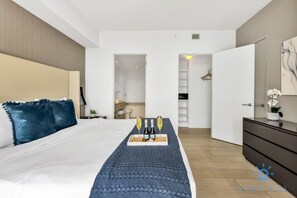 Une chambre d’hôtel moderne avec un grand lit, une table de chevet, une commode et un petit coin salon agrémenté d’un plateau de boissons.