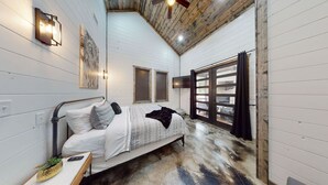 Een slaapkamer met een bed, nachtkastje, een lampje aan de muur en een raam met zonwering.