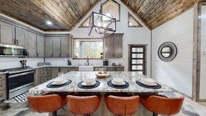 Een keuken met een groot eiland, houten plafond en een eethoek met vier stoelen.
