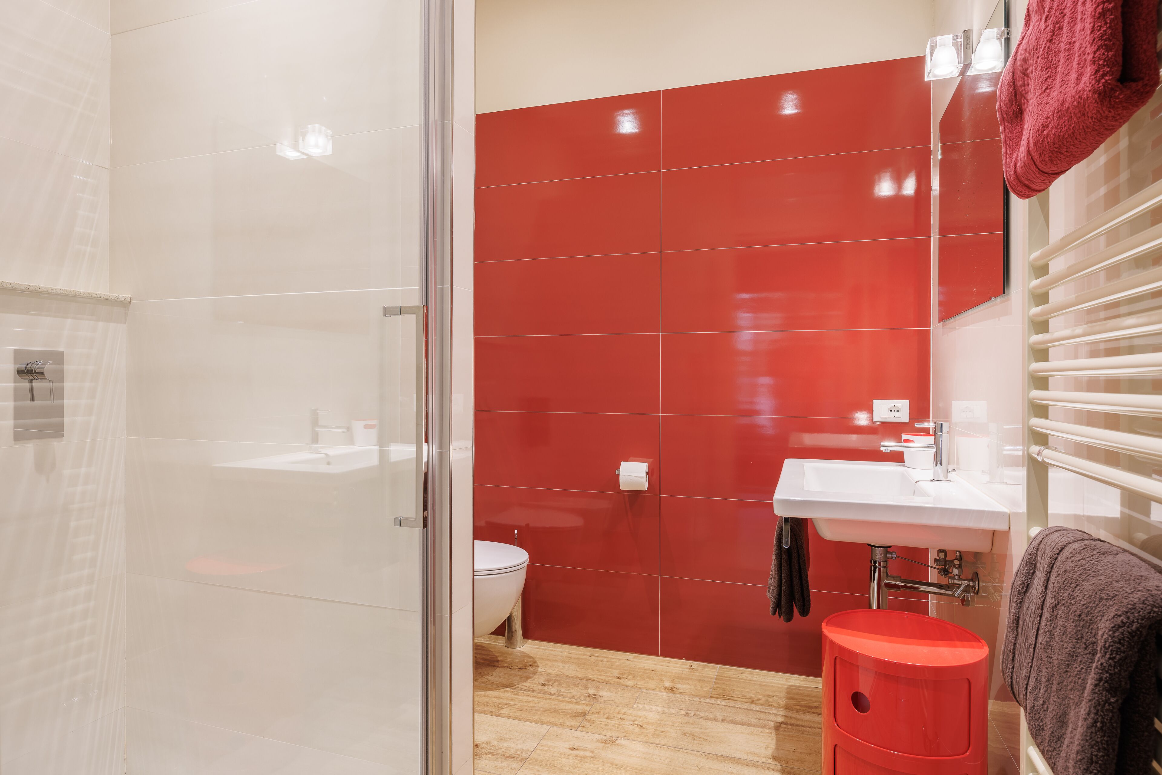 A bathroom with a glass shower enclosure, a toilet, a sink, and a red-tiled wall.
