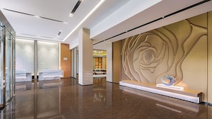 A modern hotel lobby with a marble reception desk, a seating area, and a decorative wall with abstract patterns.