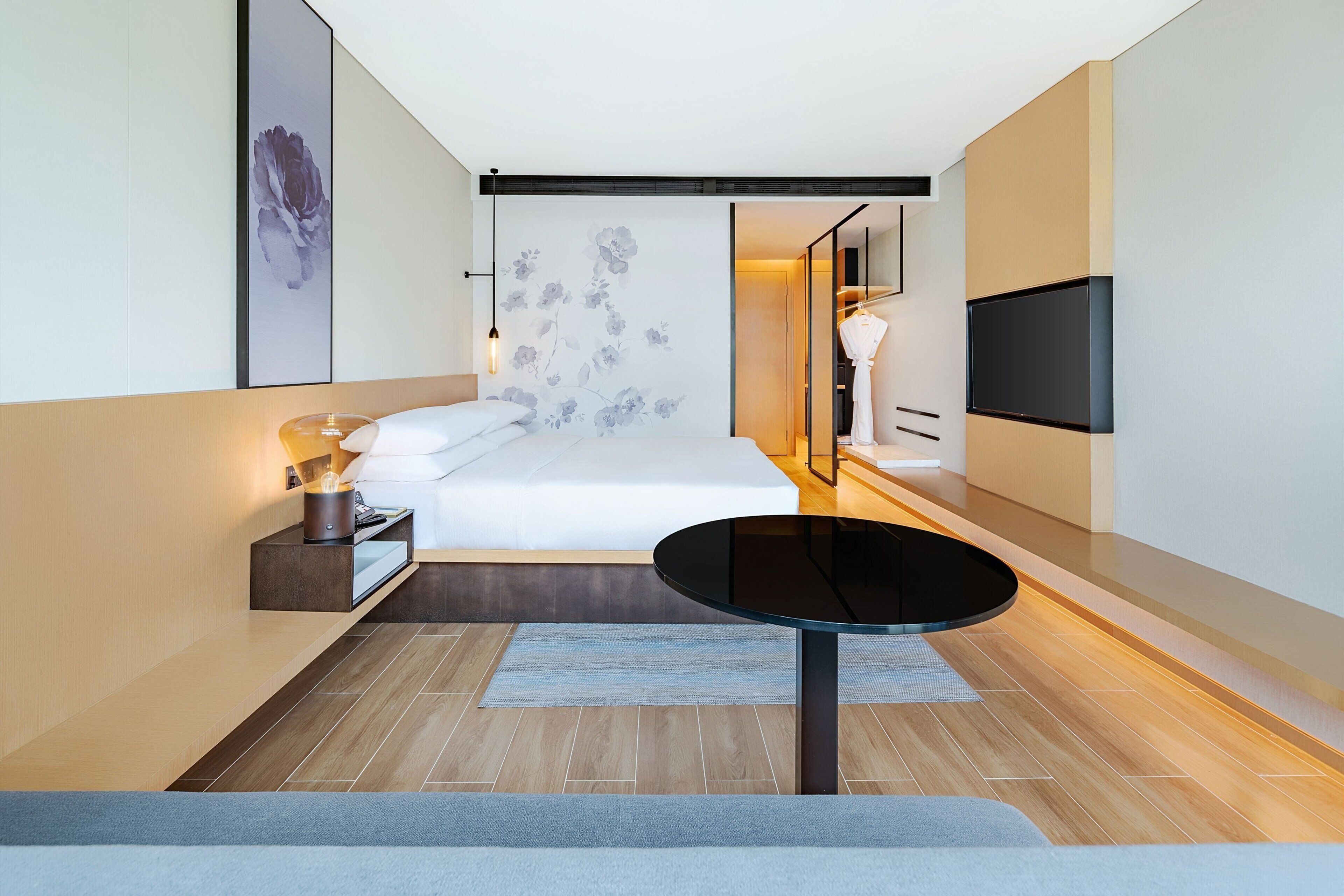 Una habitación de hotel moderna con cama, mesita de noche, lámpara y televisor de pantalla plana montado en la pared.