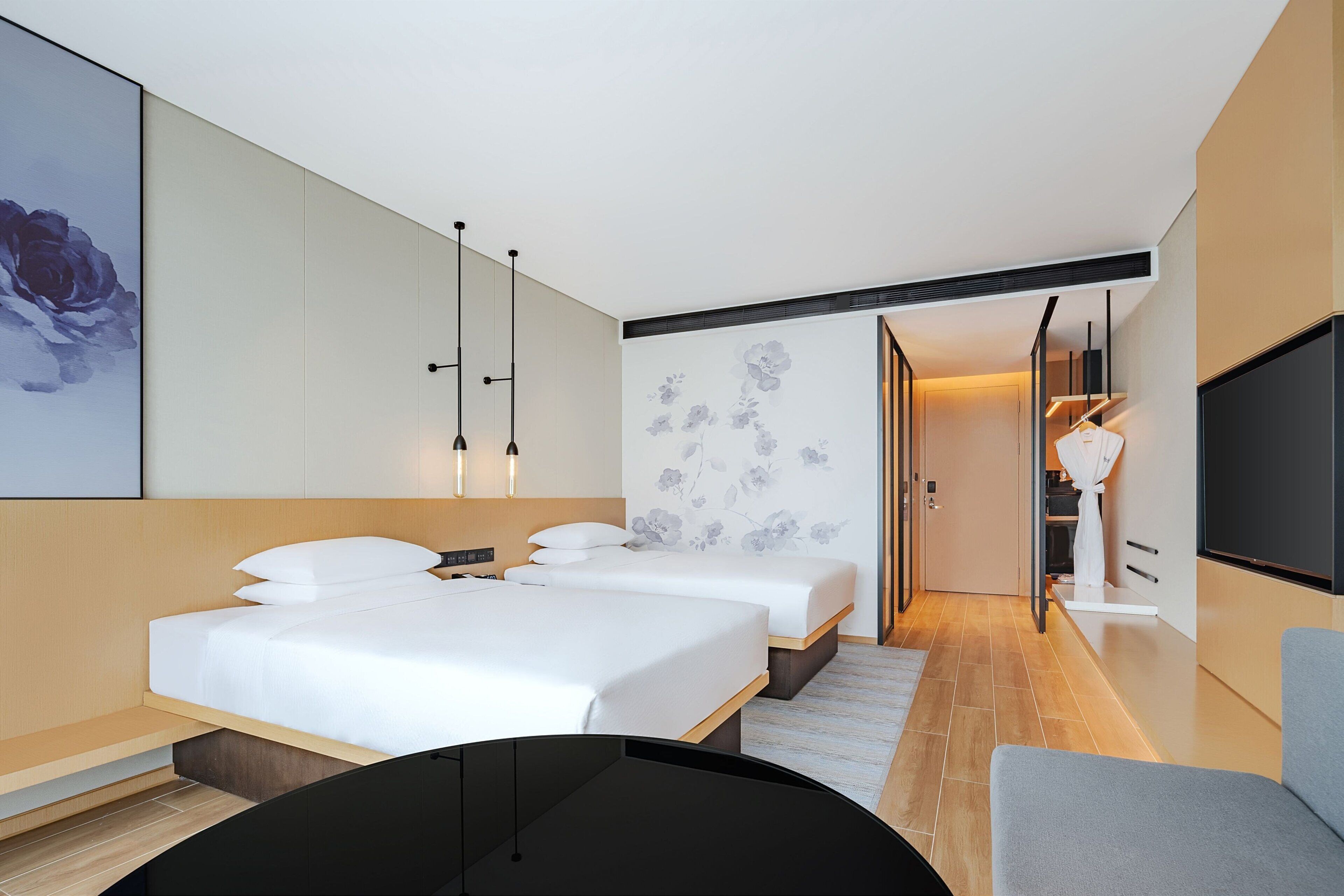 Ein modernes Hotelzimmer mit zwei Betten, einem großen Flachbildfernseher und minimalistischem Design.