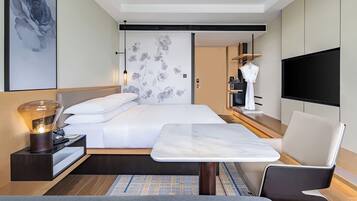 A modern hotel room with a large bed, a dining table, a TV, and a robe hanging on a rack.