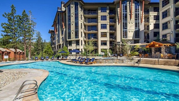 Un hotel con piscina, sillas de descanso y un patio de piedra.