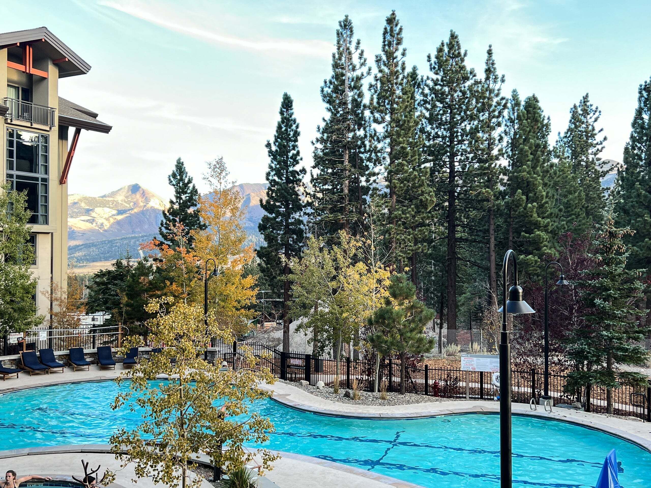 A swimming pool with a mountain backdrop, surrounded by trees and a building with a balcony.