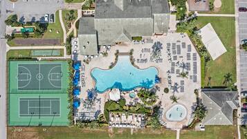 Vista aérea de un complejo turístico con una gran piscina, canchas de tenis y una zona de playa.