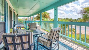 A covered outdoor seating area with striped chairs and a table, overlooking a street with palm trees and houses.