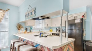 A kitchen with a central island, bar stools, white cabinets, a refrigerator, and a window with blinds.