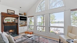 Un salon spacieux doté d’une cheminée, de grandes fenêtres et offrant une vue sur un lac.