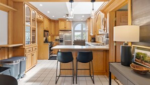Une cuisine moderne avec des meubles en bois, un îlot central, deux tabourets de bar et une grande fenêtre.