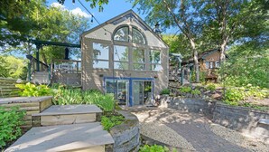 Une maison dotée d’une grande fenêtre en arc de cercle, d’une terrasse en bois et d’un chemin en pierre.