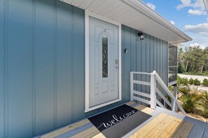 A house with a blue exterior, a white door with a number 2, a welcome mat, and a white porch railing.