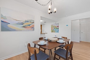 A dining area with a wooden table, chairs, and a chandelier. There are paintings on the walls. - Beach Bungalow- Perfect duplex for larger families (Fort Myers Beach)