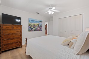 Une chambre à coucher avec un lit, une commode, un ventilateur de plafond, un tableau et une porte.