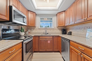 A kitchen with wooden cabinets, stainless steel appliances, a window, and a tiled backsplash.